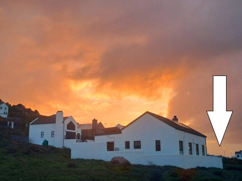 A scenic view of a residential property at sunset, featuring white exterior walls, a chimney, and roof-mounted solar panels.