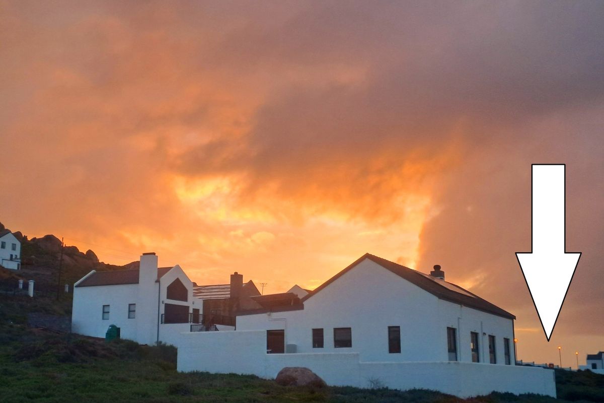 A scenic view of a residential property at sunset, featuring white exterior walls, a chimney, and roof-mounted solar panels.