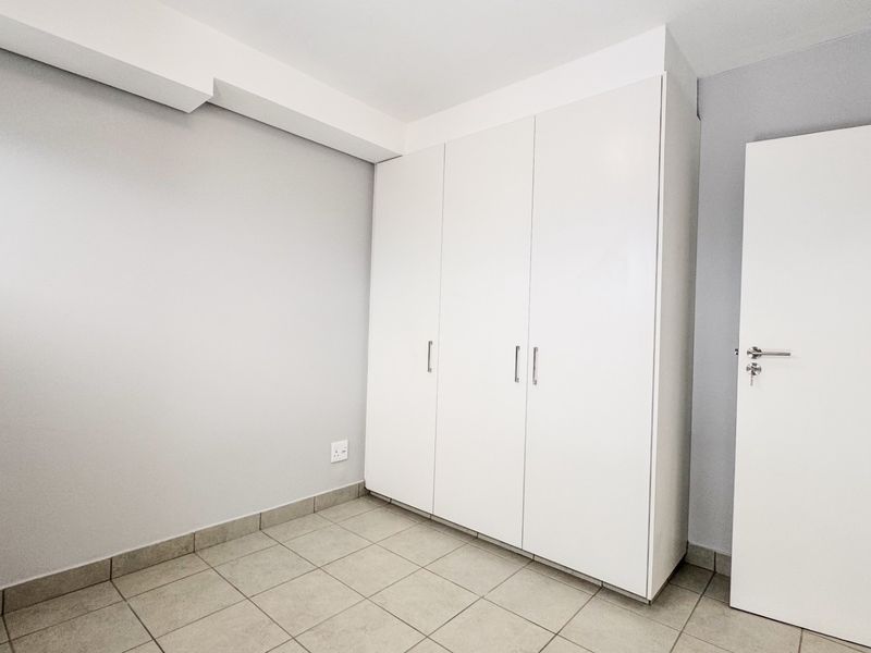 A clean, empty bedroom featuring neutral tiled flooring and white built-in cupboards, offering a versatile space ready for personalization.