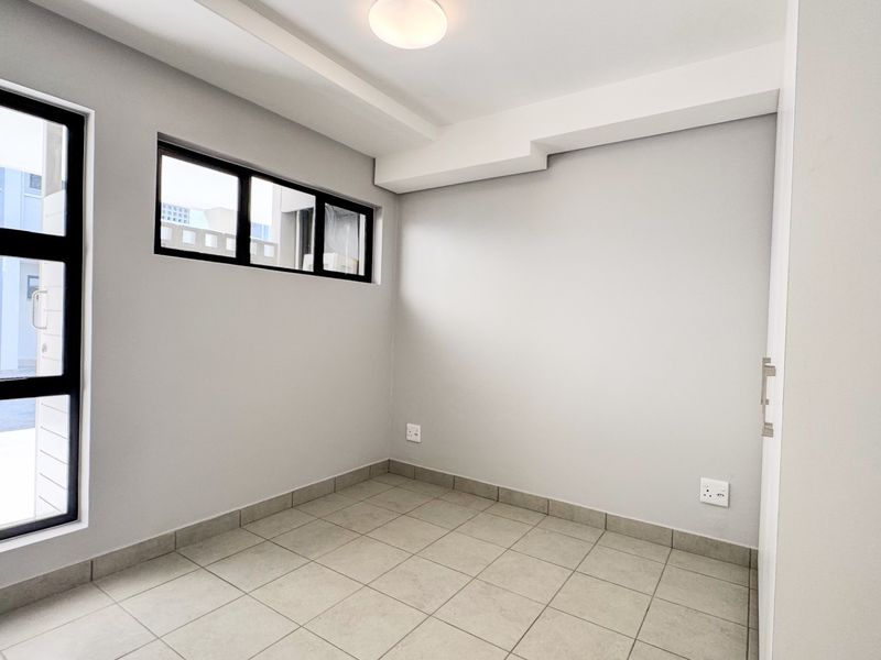 A clean, empty bedroom featuring neutral tiled flooring, modern aluminium-framed windows, and a minimalist aesthetic, ready for personalization.