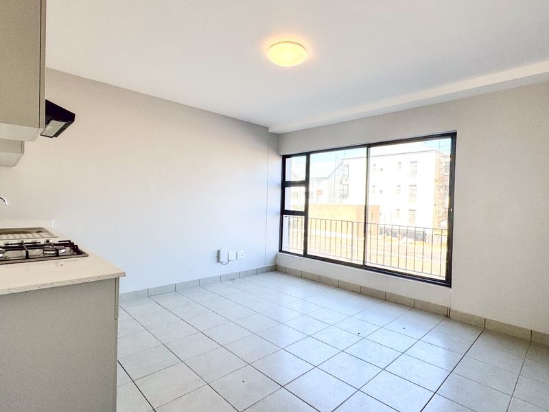 An open-plan kitchen and living area featuring tiled floors, built-in cabinetry with a gas hob, and a large sliding door leading to a balcony.