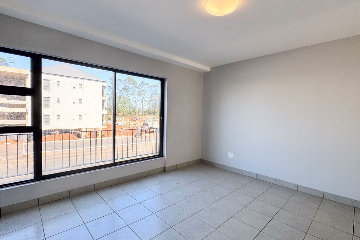 A bright, empty bedroom featuring neutral tiled flooring, clean walls, and a large sliding window providing natural light and an exterior view.