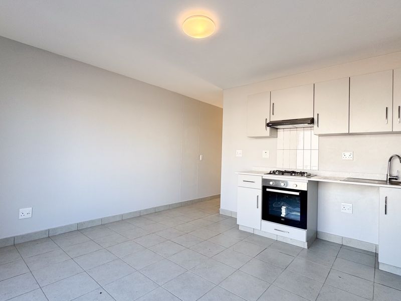 An open-plan kitchen and living area featuring tiled flooring, built-in cabinetry, and integrated cooking appliances in a clean, neutral space.