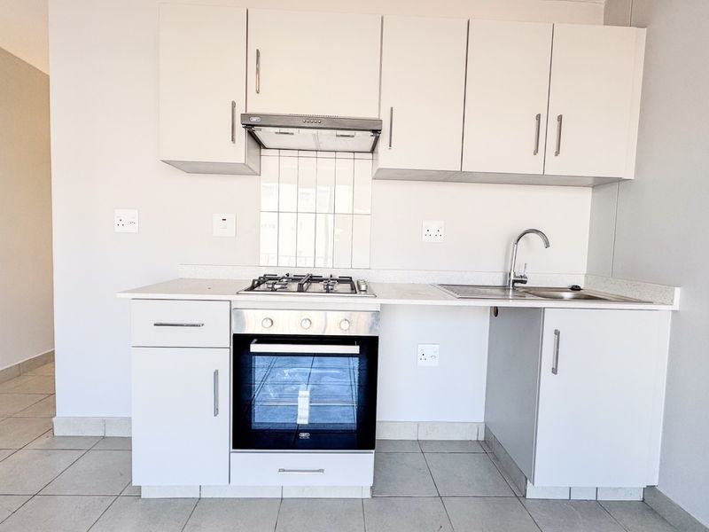 A clean, modern kitchen featuring white cabinetry, a gas hob, built-in oven, extractor fan, and stainless steel sink with tiled splashback.