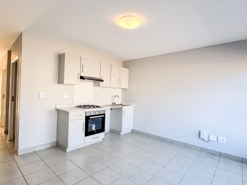 An open-plan kitchen area featuring white built-in cabinetry, a gas hob, an electric oven, and tiled flooring in a clean, vacant space.