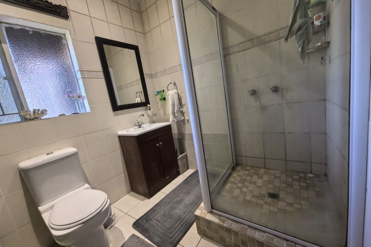 A functional bathroom featuring a shower enclosure, vanity cabinet, and toilet, with tiled finishes throughout. The space would benefit from cosmetic updates.