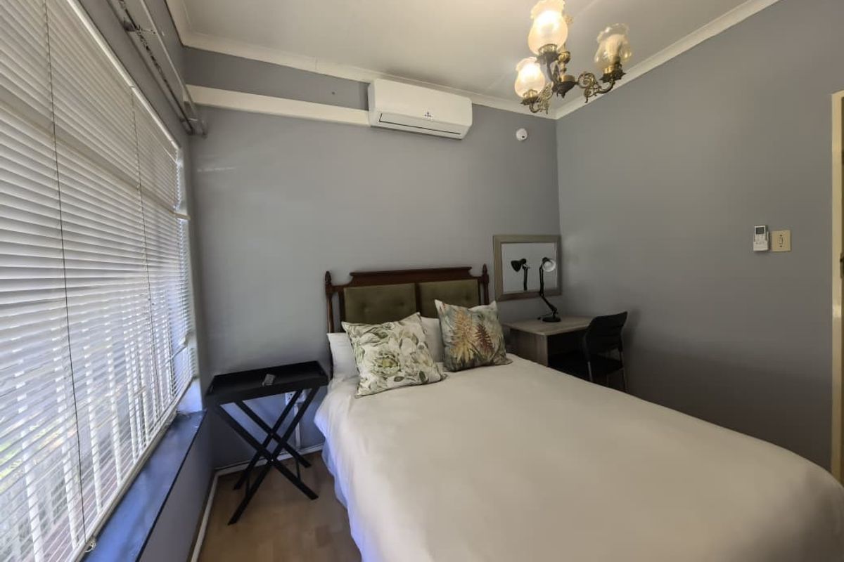 A well-lit bedroom featuring laminate flooring, a split-system air conditioner, and venetian blinds, offering a comfortable and functional living space.