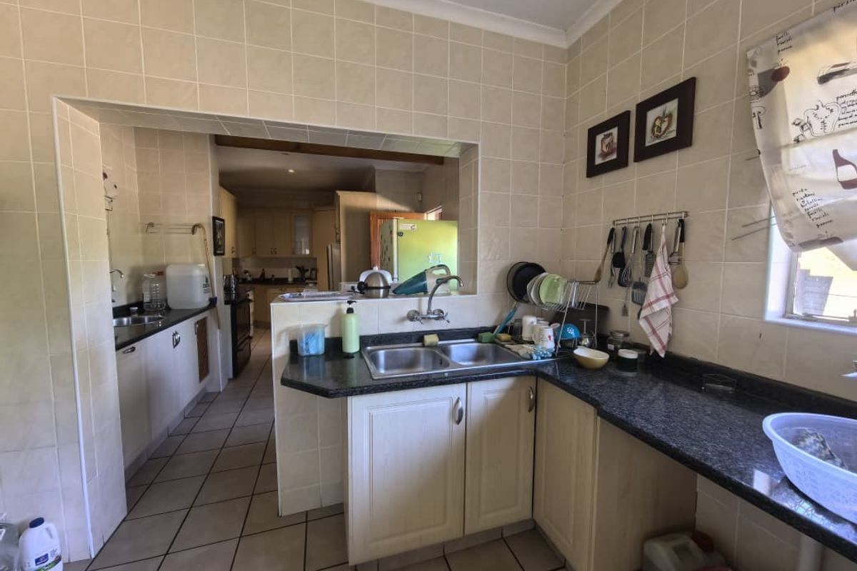 A functional kitchen featuring granite countertops, double bowl sink, tiled splashbacks, and tiled flooring, with an open-plan layout connecting to an adjacent prep area.