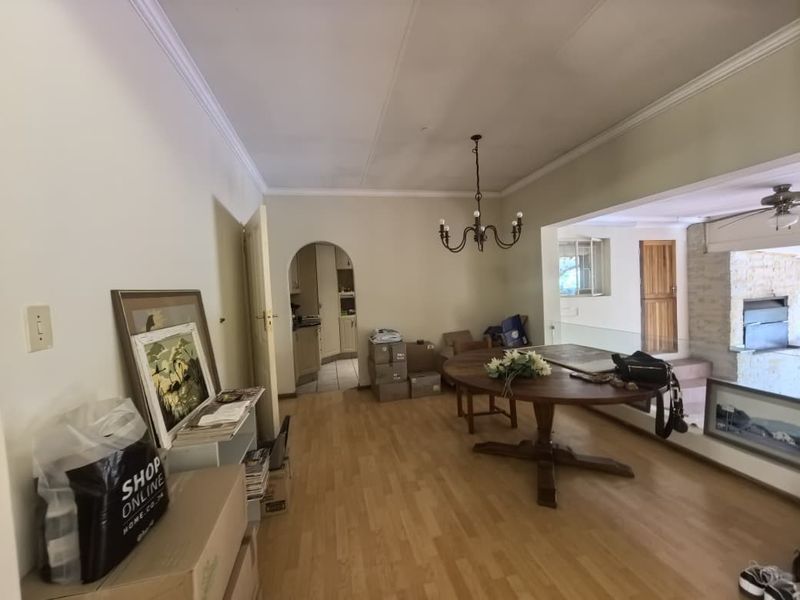 Open plan living and dining area featuring laminate flooring, coved ceilings, and an arched entryway leading to the kitchen.