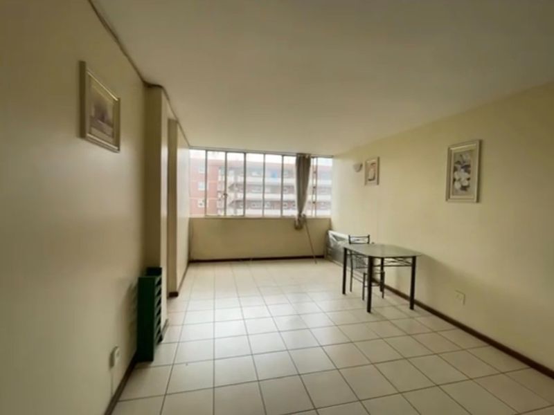 A spacious, neutrally painted living area featuring tiled flooring and a large window that provides ample natural light.