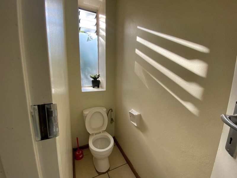 A compact, functional bathroom featuring a standard toilet, tiled flooring, and a louver window providing natural light.