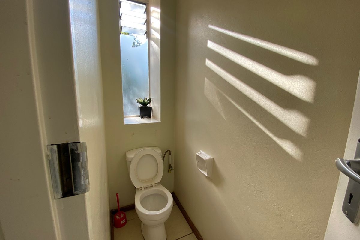 A compact, functional bathroom featuring a standard toilet, tiled flooring, and a louver window providing natural light.