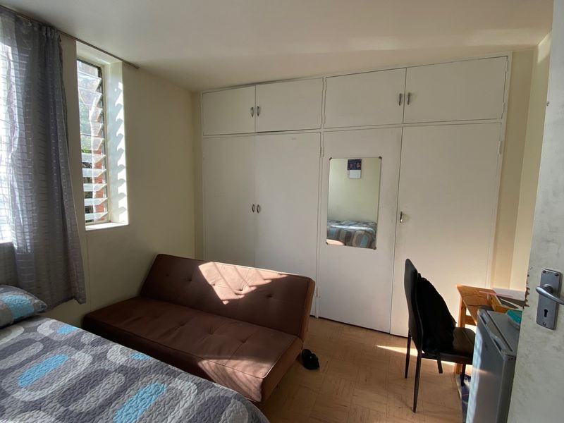 A bedroom featuring built-in cupboards, parquet flooring, and a louver window providing natural light.