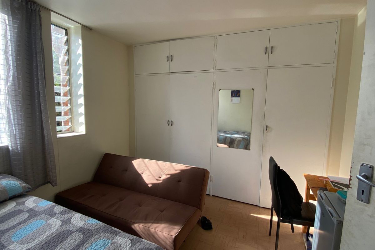 A bedroom featuring built-in cupboards, parquet flooring, and a louver window providing natural light.