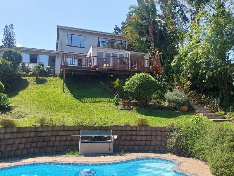 Rear view of the property featuring a swimming pool, a raised wooden deck, and a landscaped garden with stone stairs leading up to the house.