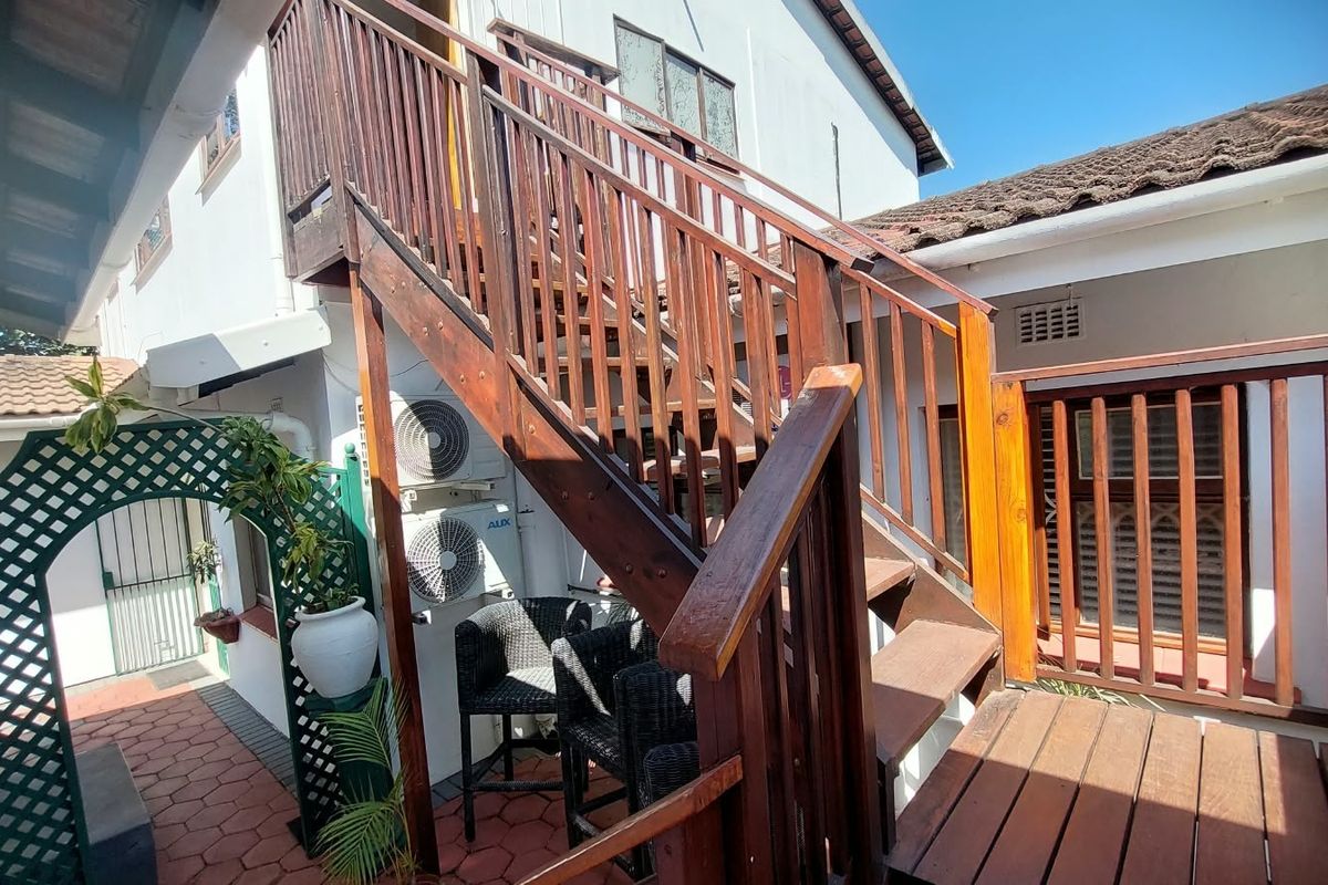 Rear exterior view featuring a wooden staircase leading to an upper level, paved patio area, and wall-mounted air conditioning units.