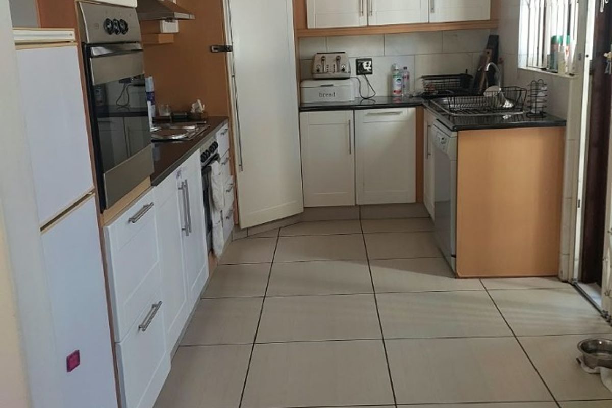 A functional kitchen featuring built-in cabinetry, granite countertops, integrated oven and hob, and tiled flooring with natural light from the side window.