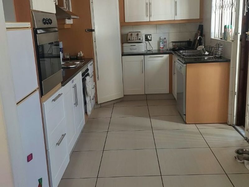 A functional kitchen featuring built-in cabinetry, granite countertops, integrated oven and hob, and tiled flooring with natural light from the side window.