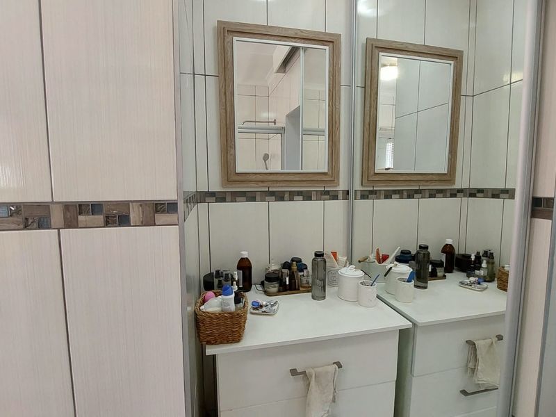 A functional bathroom vanity area featuring white cabinetry, dual wall-mounted mirrors, and decorative mosaic tile accents on the wall.