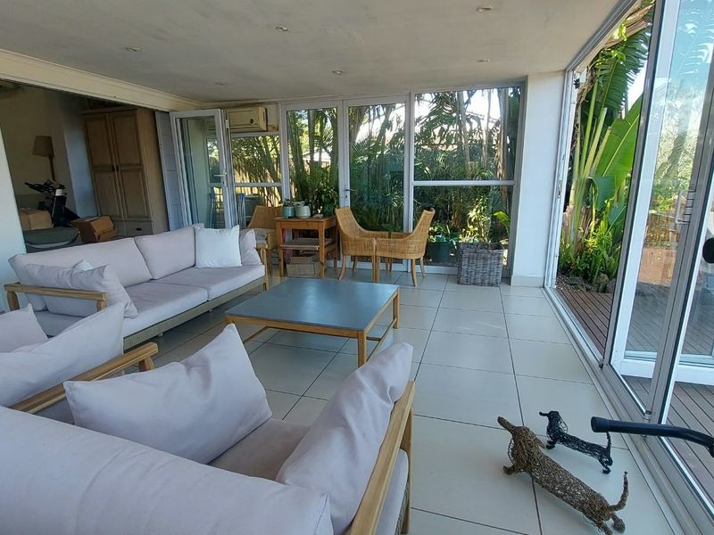 A bright, enclosed patio featuring large sliding glass doors, tiled flooring, and recessed lighting, offering a seamless transition to the outdoor garden area.