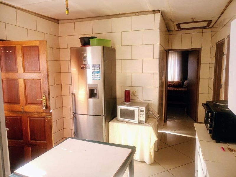 A dated kitchen area featuring tiled walls and flooring, requiring significant renovation and repair to the ceiling and finishes.