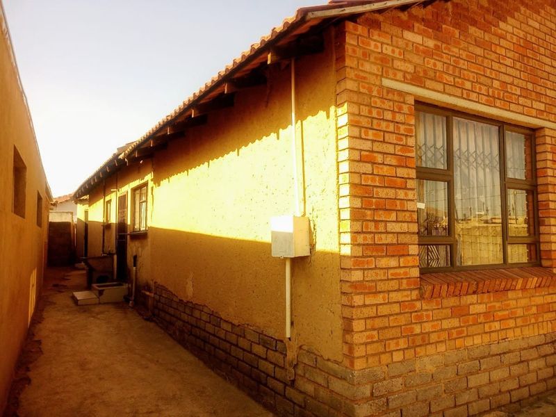 A side view of the property showing a brick and plastered exterior wall, tiled roof, and a concrete pathway along the side of the house.