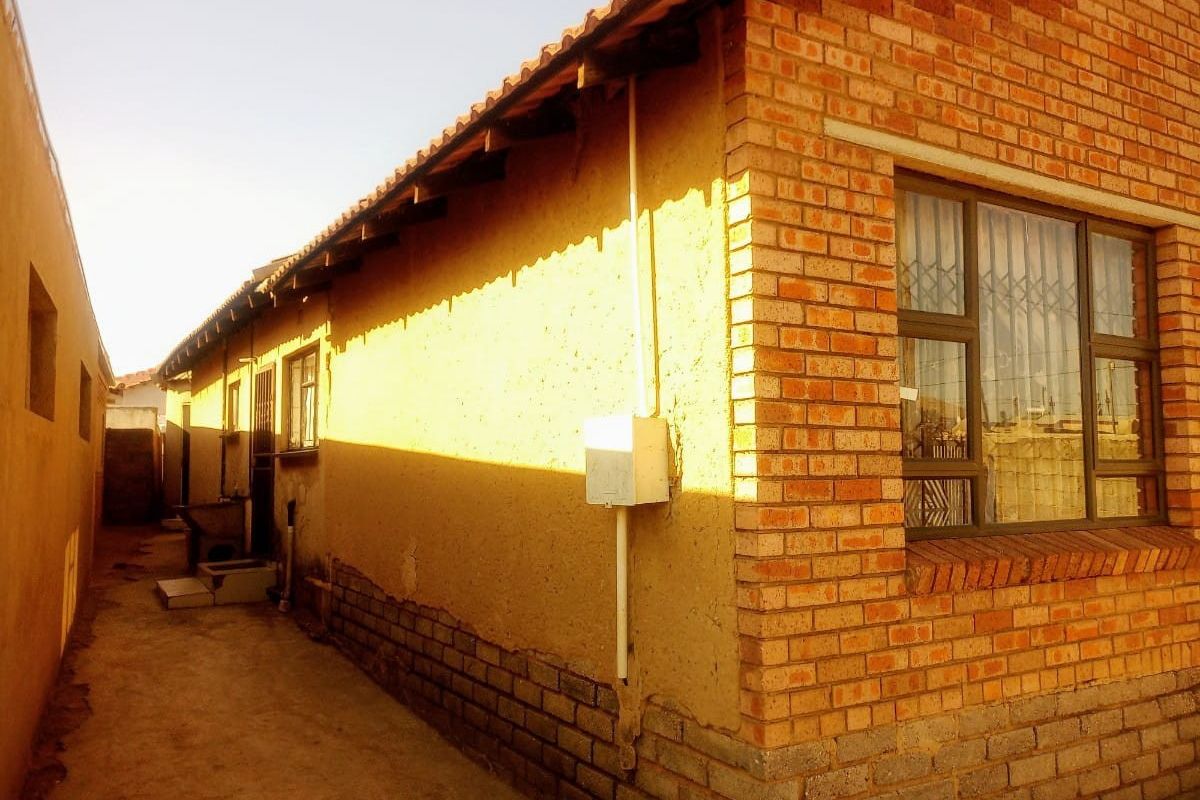 A side view of the property showing a brick and plastered exterior wall, tiled roof, and a concrete pathway along the side of the house.