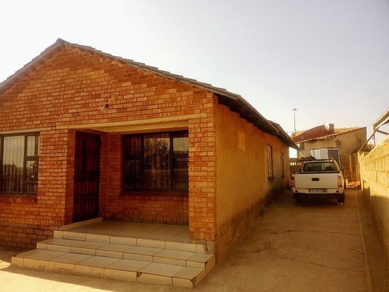 Front view of a face brick house featuring a small covered entrance with tiled steps and a concrete driveway leading to the side.