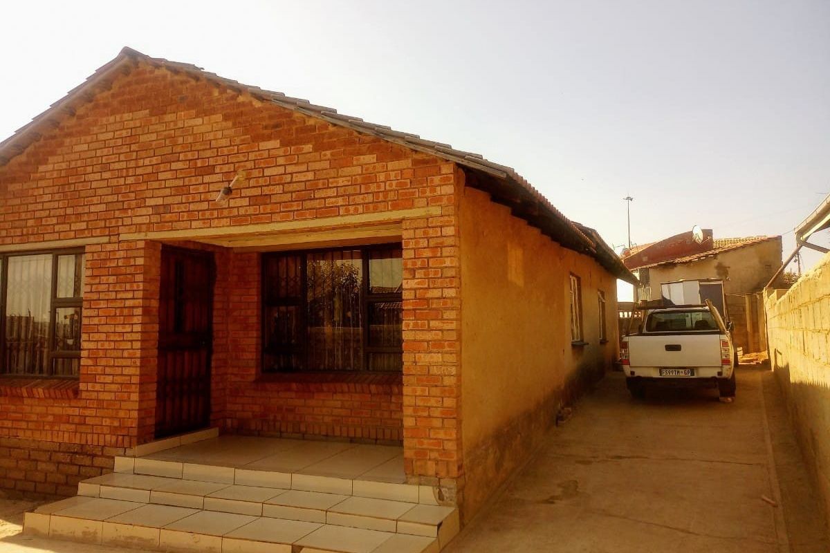 Front view of a face brick house featuring a small covered entrance with tiled steps and a concrete driveway leading to the side.