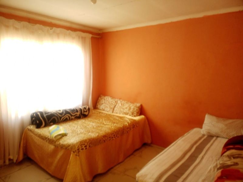 A bedroom featuring tiled flooring and a large window with curtain fittings, currently finished with bright orange wall paint.