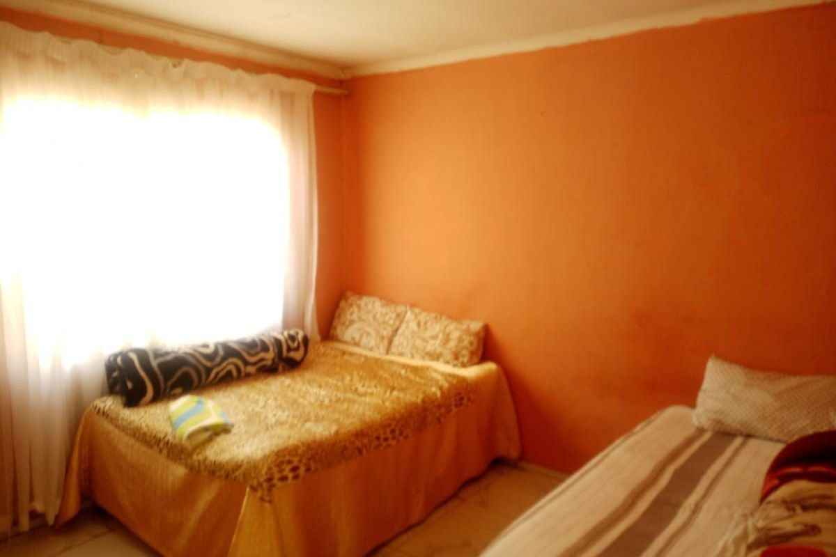 A bedroom featuring tiled flooring and a large window with curtain fittings, currently finished with bright orange wall paint.