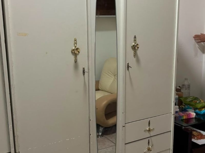 A bedroom featuring a large, dated built-in wardrobe with a central mirror and tiled flooring.