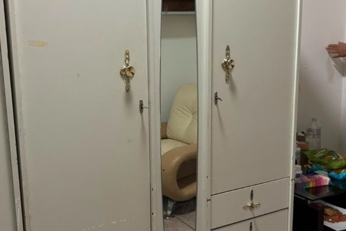 A bedroom featuring a large, dated built-in wardrobe with a central mirror and tiled flooring.