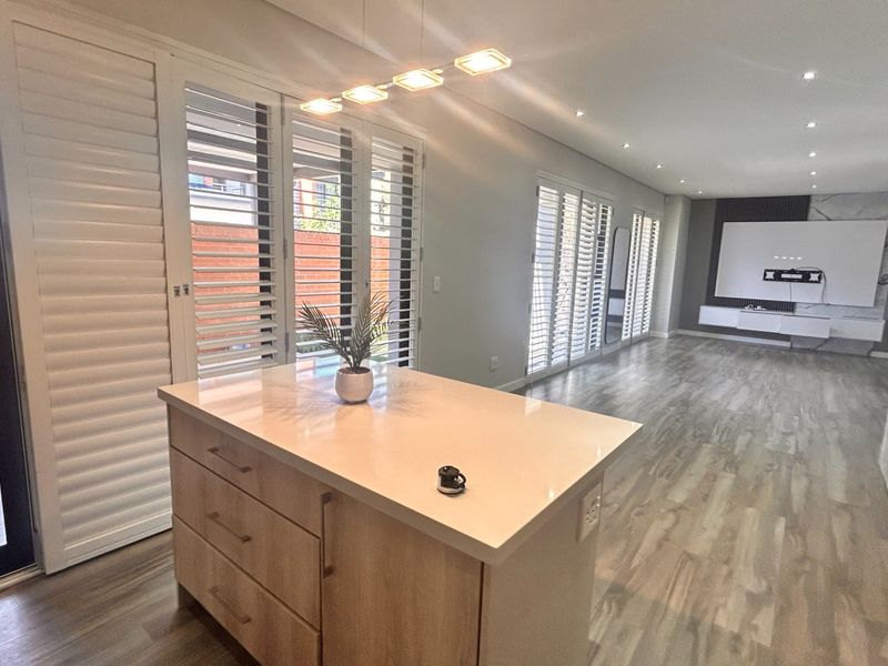 Spacious open-plan living area featuring a modern kitchen island with quartz countertop, plantation shutters, and sleek laminate flooring throughout.