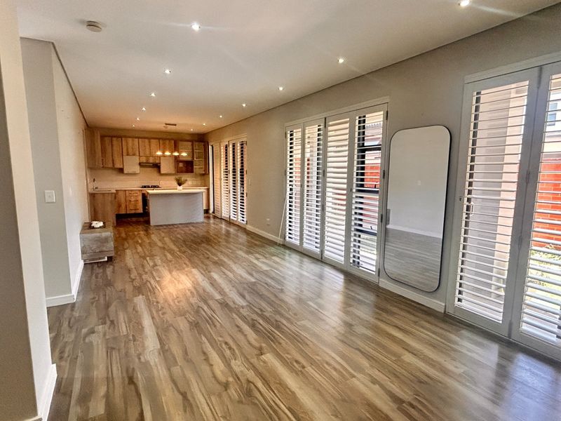 Spacious open-plan living and kitchen area featuring modern laminate flooring, recessed lighting, and plantation shutters, offering a bright and versatile layout.