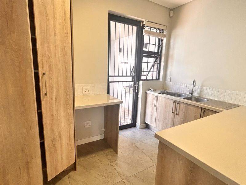 A clean and functional laundry area featuring light wood-finish cabinetry, ample counter space, a stainless steel sink, and direct access to an outdoor area.