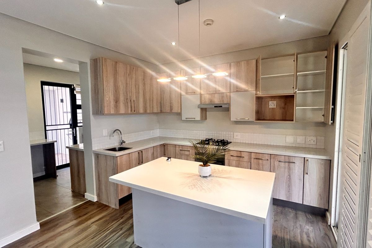 Modern kitchen featuring light wood-tone cabinetry, stone countertops, a central island, and integrated gas hob with extractor fan.