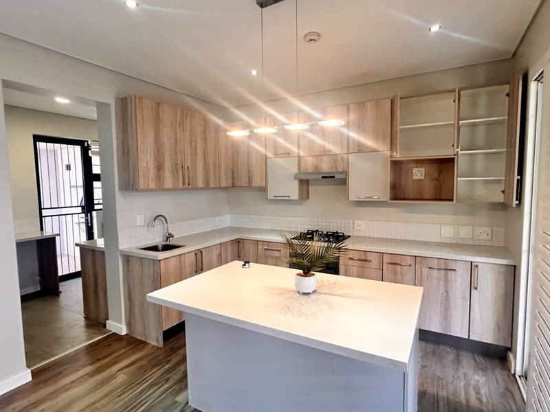 Modern kitchen featuring light wood-tone cabinetry, stone countertops, a central island, and integrated gas hob with extractor fan.