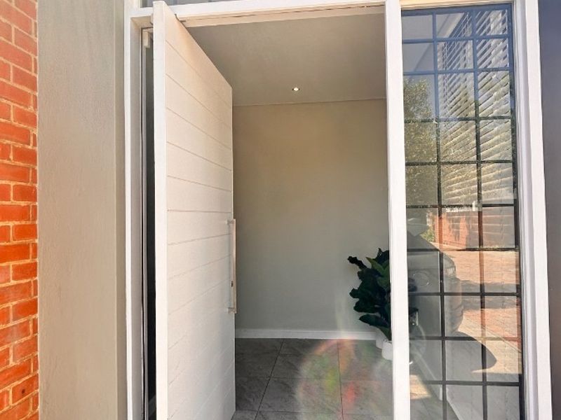 Modern townhouse entrance featuring a large white panel door with glass sidelights and transom window, leading into a clean, tiled interior space.