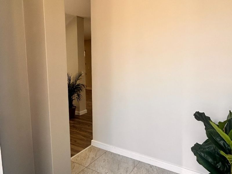 A clean and modern hallway featuring neutral wall tones, tiled flooring, and recessed downlighting, leading into the main living area.
