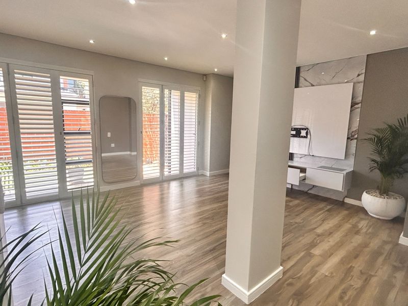 Spacious living area featuring modern laminate flooring, plantation shutters, recessed lighting, and a sleek built-in media console with a marble-look feature wall.