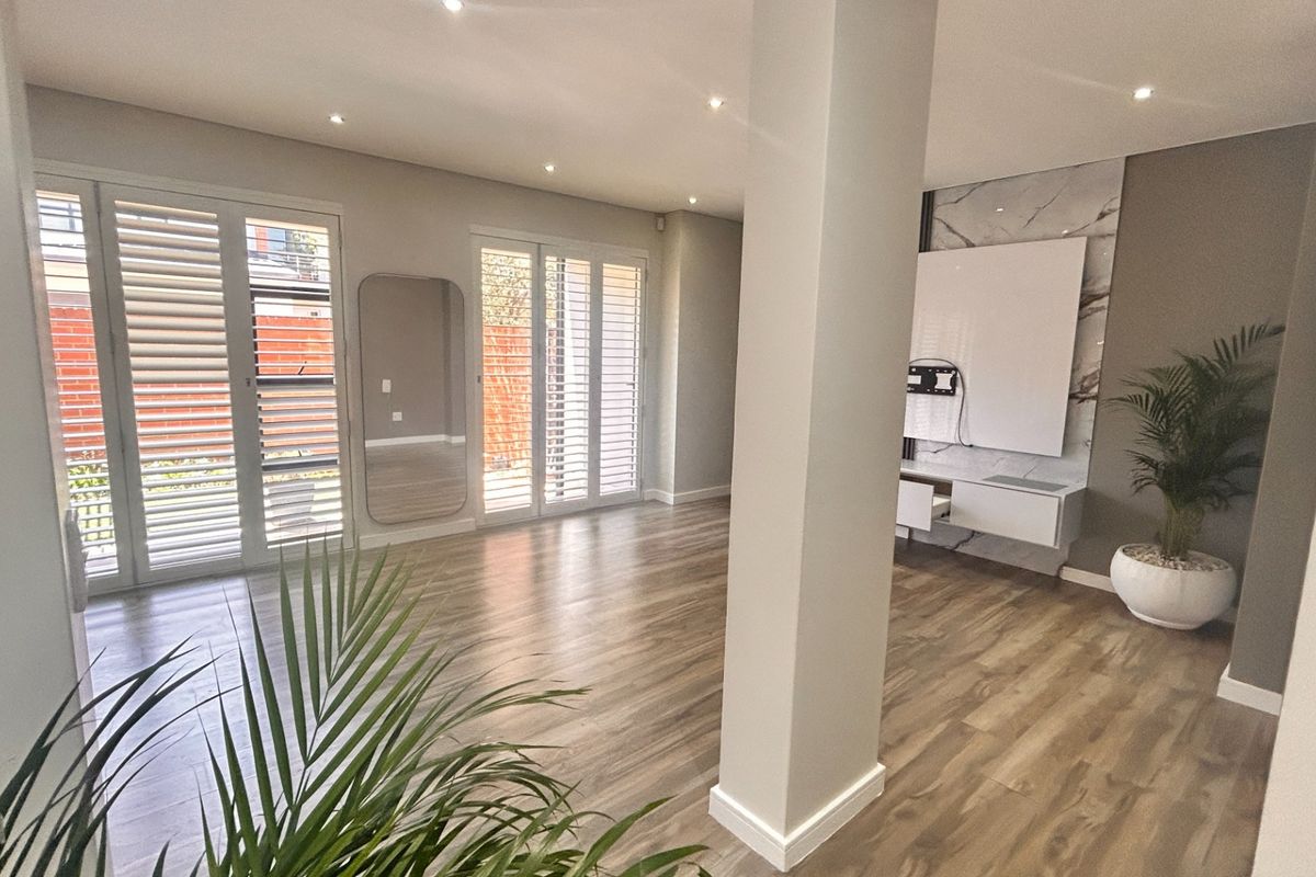 Spacious living area featuring modern laminate flooring, plantation shutters, recessed lighting, and a sleek built-in media console with a marble-look feature wall.