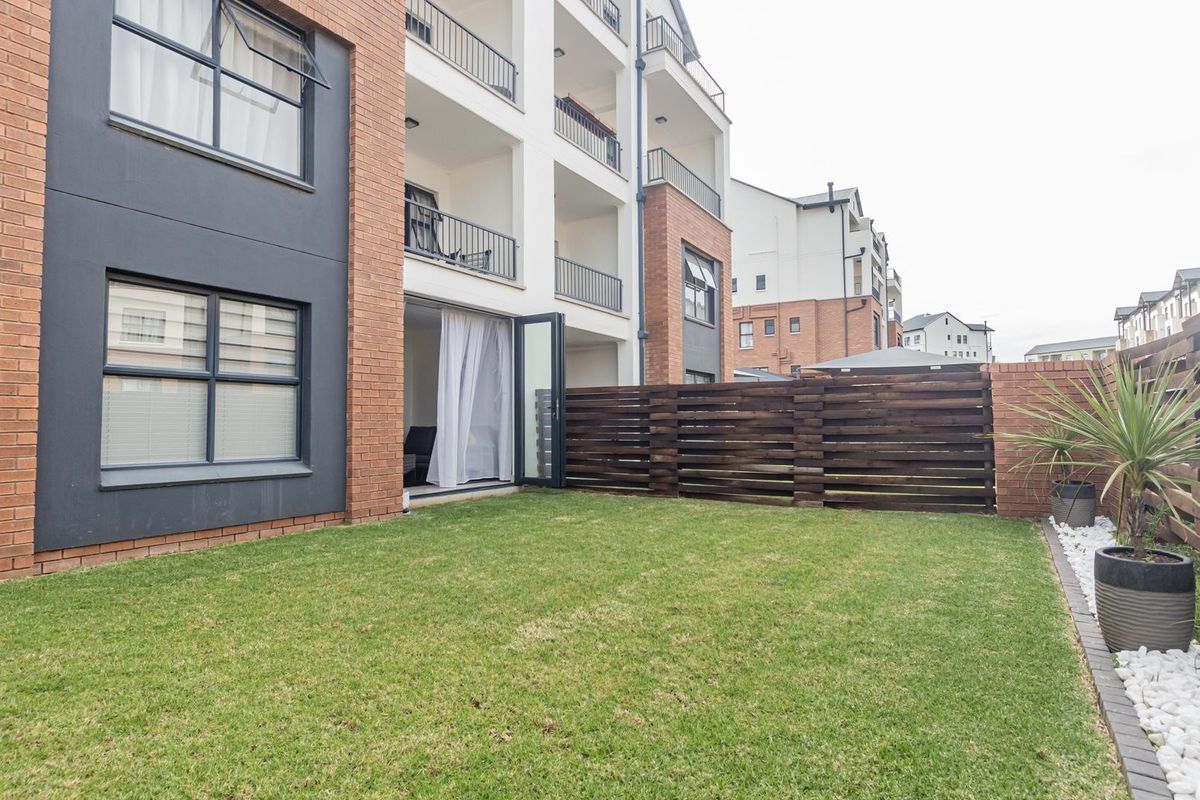 A private rear garden area featuring a well-maintained lawn, decorative pebble border, and timber fencing, adjacent to the apartment building's ground floor patio.