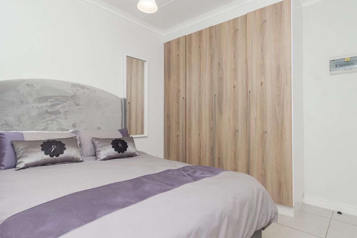 A well-maintained bedroom featuring modern wood-finish built-in cupboards and neutral wall tones.