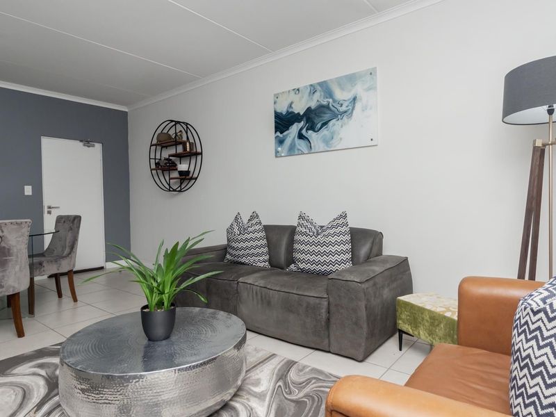 A well-maintained open-plan living and dining area featuring neutral tiled flooring, clean white walls, and modern recessed lighting.