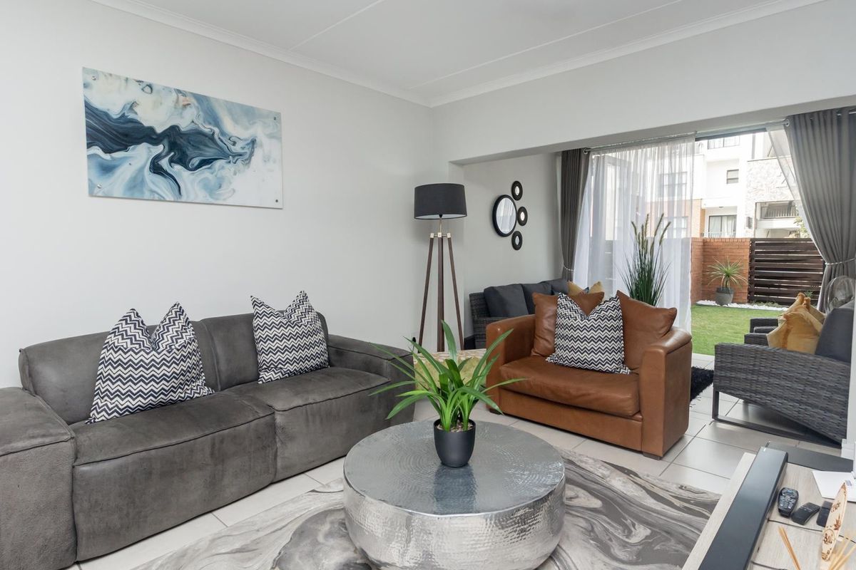 A bright and well-maintained living room featuring tiled flooring and a large sliding glass door providing direct access to the outdoor patio area.