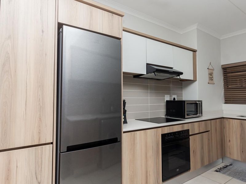 Modern kitchen featuring light wood-grain cabinetry, sleek white countertops, a tiled backsplash, and integrated appliances including an oven and extractor fan.