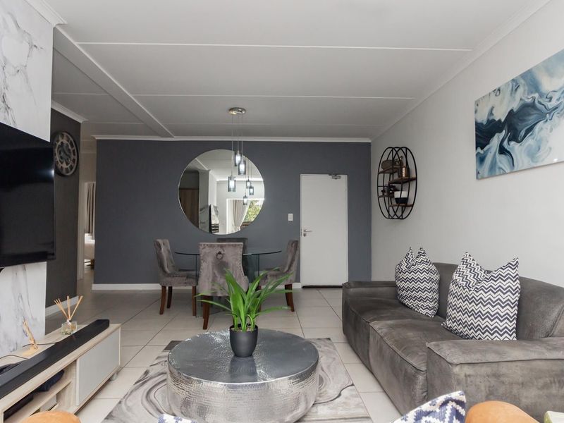 A modern open-plan living and dining area featuring tiled floors, a marble-look feature wall, and contemporary pendant lighting.