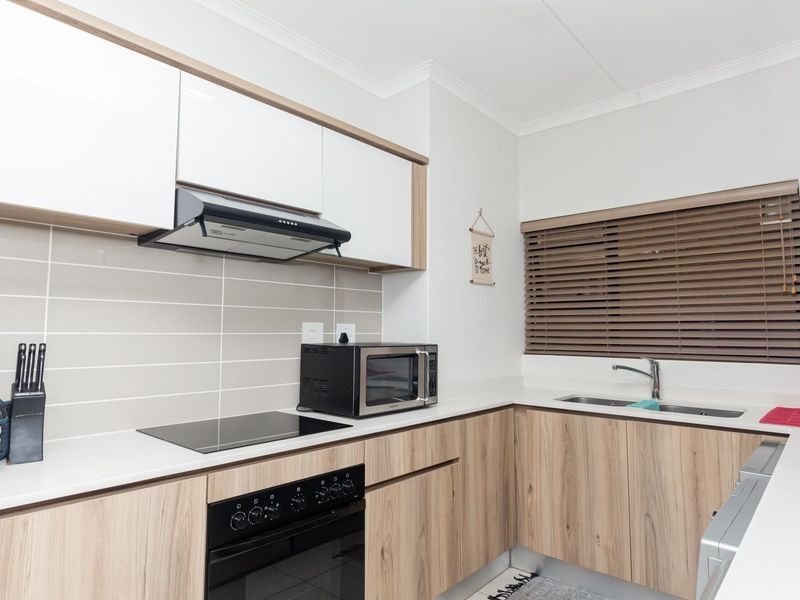Modern kitchen featuring light wood-grain cabinetry, stone countertops, a sleek ceramic backsplash, and integrated appliances including a hob, oven, and double basin sink.
