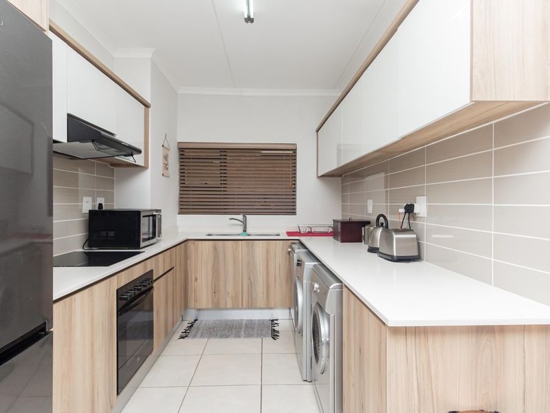 Modern galley-style kitchen featuring light wood-grain cabinetry, white stone countertops, tiled backsplash, and integrated appliances including an oven and hob.
